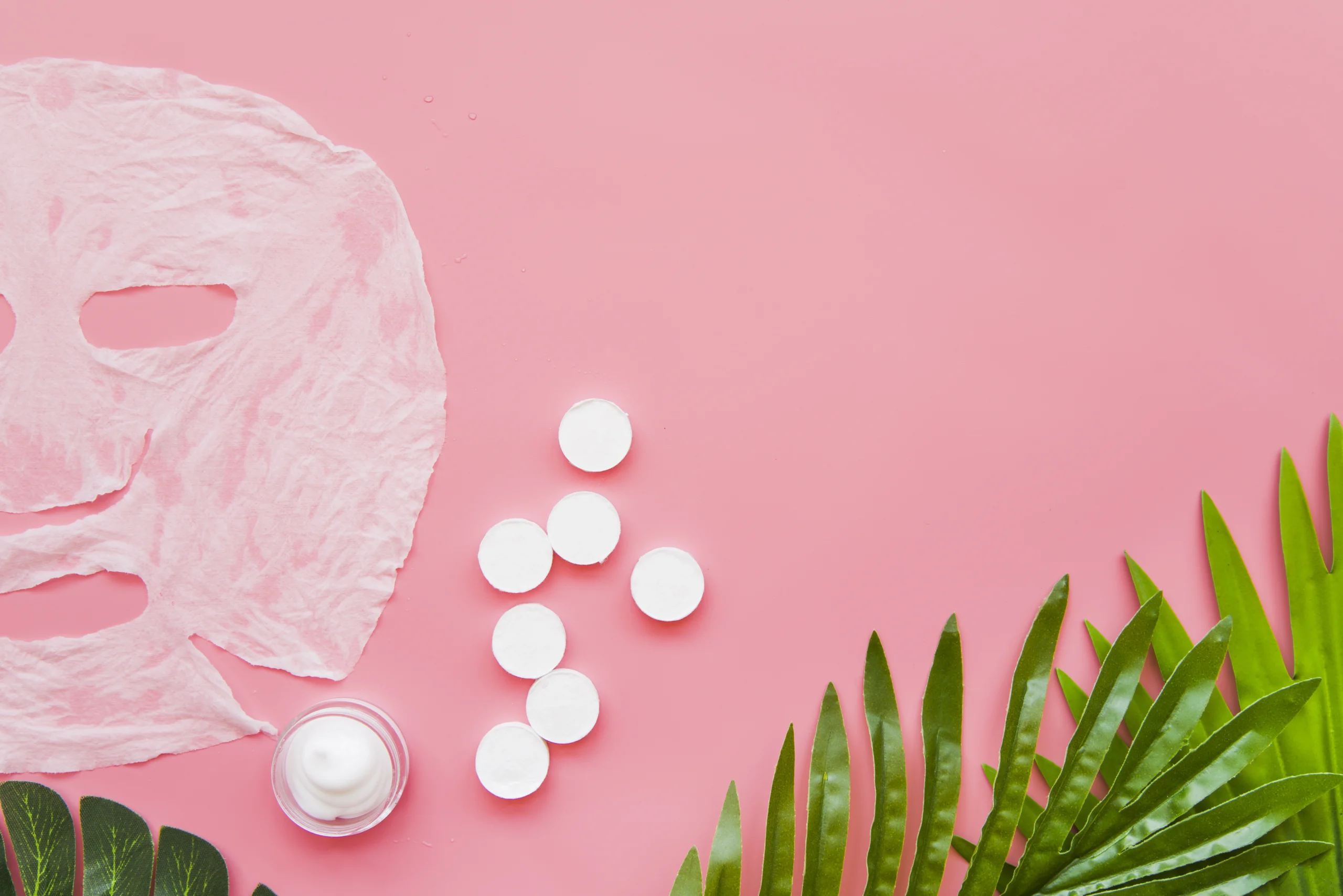 Maschera in tessuto su sfondo rosa, con candele, crema viso e foglie